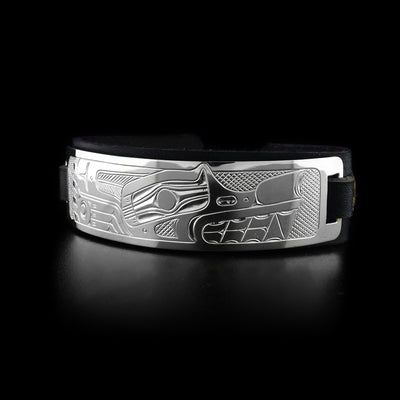 Leather cuff has sterling silver plate with side-view of wolf’s head and paw. Design is done in ovoids, lines and cross-hatching. Leather is black.
