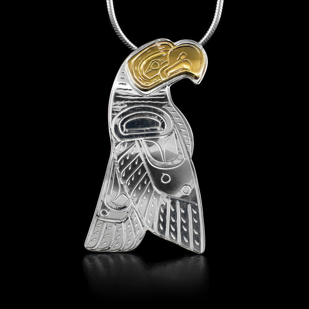 This silver and 14K gold pendant is shaped like the Eagle and has carvings that depict the Eagle. The Eagle's face is made of 14k gold.