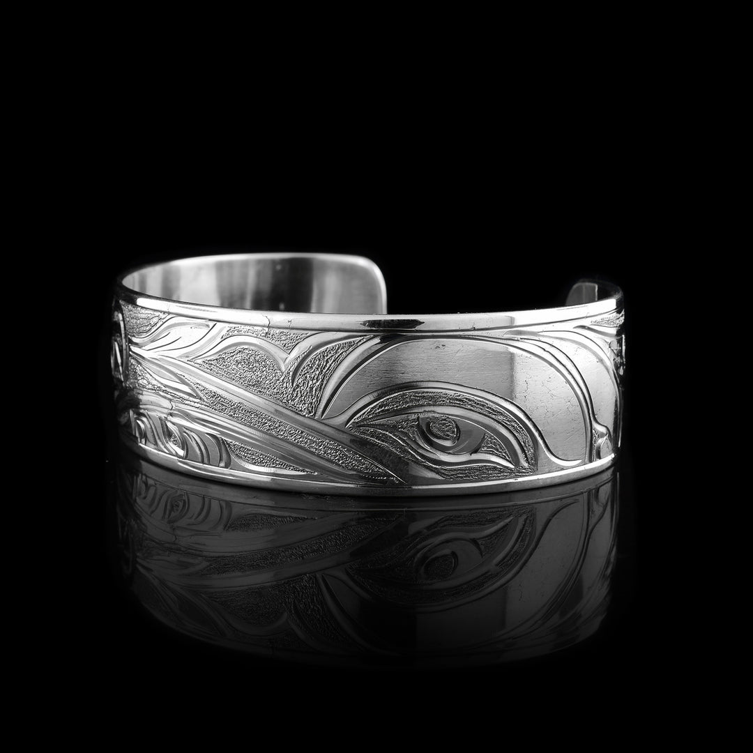 This sterling silver cuff bracelet features a detailed design of a hummingbird and a wolf. The hummingbird is shown in graceful motion, while the wolf is depicted with bold, stylized features. Together, they create a striking piece that symbolizes balance and harmony in nature.