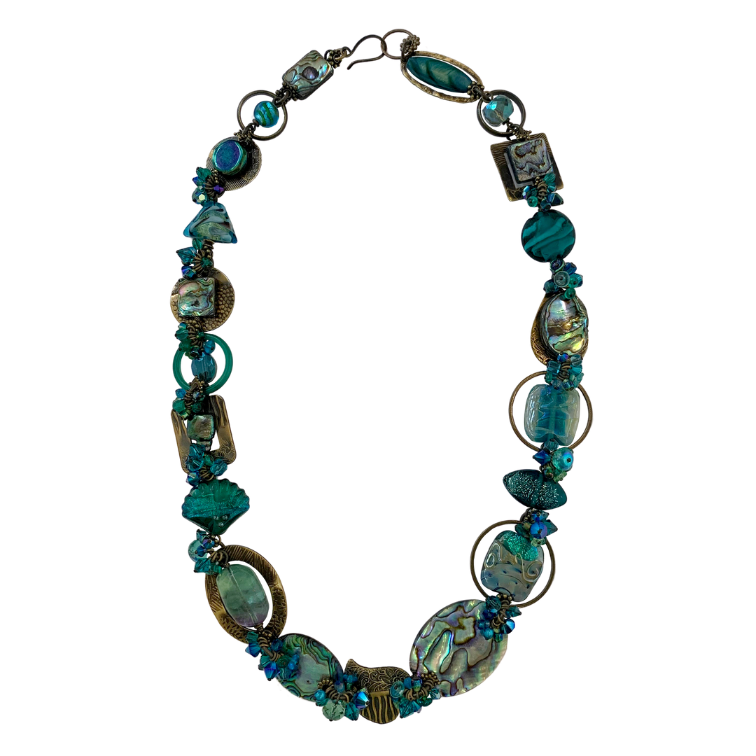 This gemstone bead necklace is made from reshwater pearls, glass beads, hand worked brass, dyed agate, pressed glass, kyanite, fluorite, and dyed shell. The piece features large beads of various different materials and shapes.