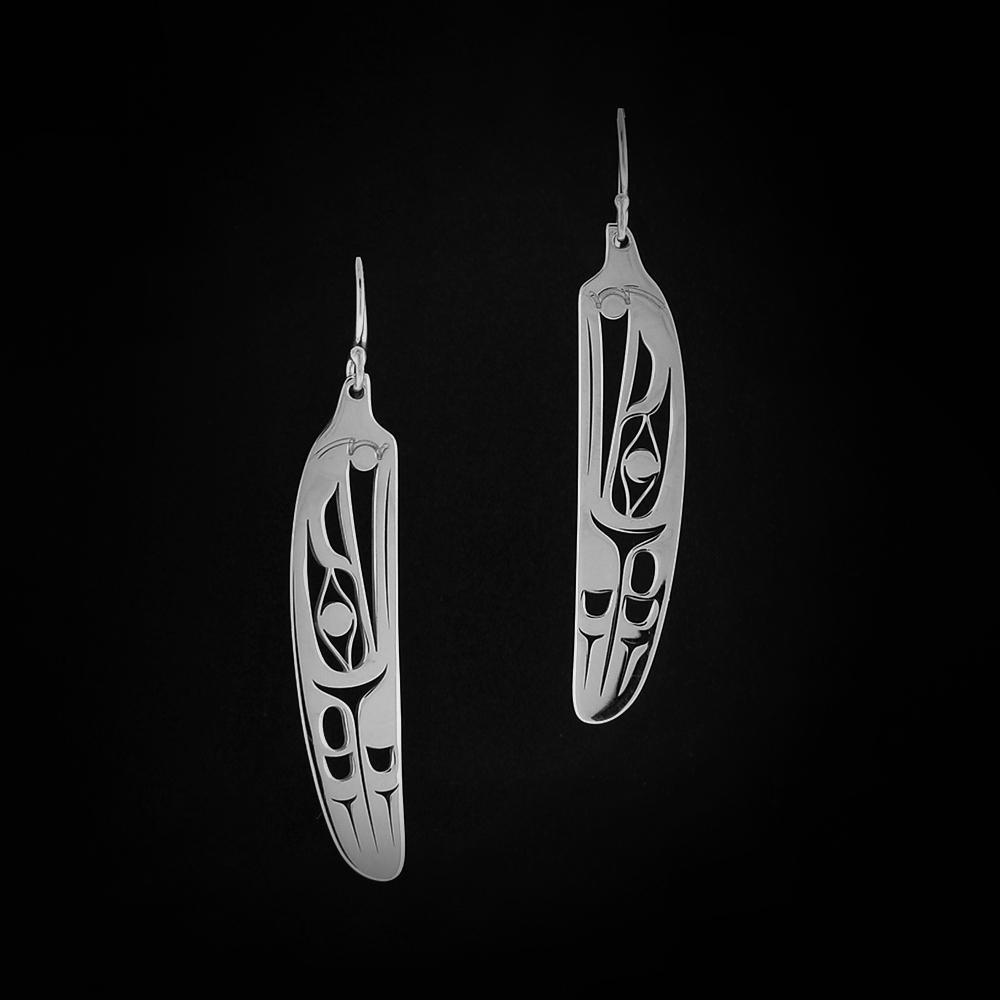 Sterling silver Raven feather earrings by Grant Pauls. Each earring is in the shape of a bird feather. Within each earring the artist has cut out the profile of a raven's head with a sun in its beak facing upward. Following the raven's head, there are intricate designs representing the feathers of the raven.