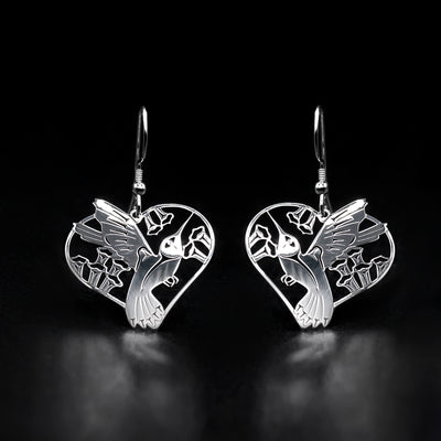 Sterling Silver Hummingbird Heart Earrings by Grant Pauls. Each earring is in the shape of a hummingbird. The artist has laser cut the profile of a full-bodied hummingbird mid-flight drinking from some flowers in the center of the pendant. 