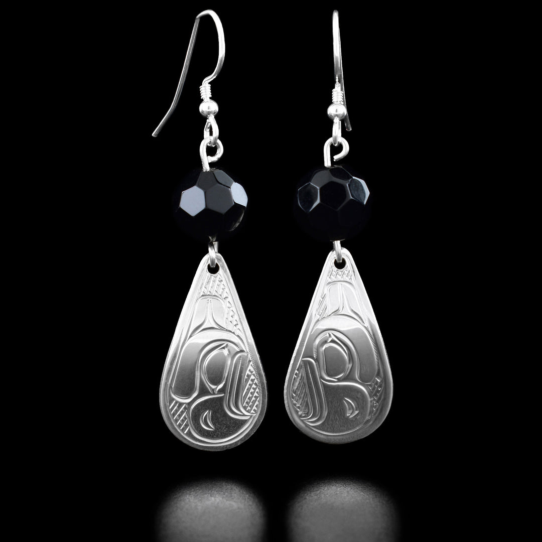 Sterling Silver Eagle Earrings with Tourmaline by Victoria Harper. Underneath the hook are two, sphere-like tourmaline gemstones and underneath hand teardrop sterling silver earrings. On each of those earrings is a profile of an eagle's head looking downward. The eagle has a pointy beak and a feather on the back of its head. The background has been hand-carved by the artist in a crisscross pattern to allow for the eagle to stand out.