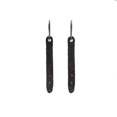 These oxidized earrings are long, dark grey, and have a course texture. There are 3 linear gemstones near the bottom of each earring. 