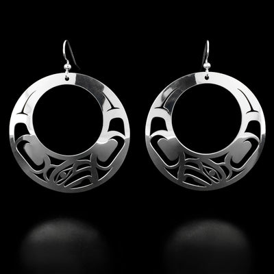 Sterling Silver Large Offset Eagle Earrings by Grant Pauls. The design of each earrings depicts the profile of an eagle's head at the very bottom of the earrings. The artist has cutout a large circle in the middle of each earring with intricate designs surrounding it.