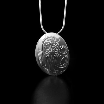 Sterling Silver Oval Raven Pendant by Don Lancaster. The design of the pendant depicts the profile of a raven's head facing downwards. The artist has hand-carved a wing to the right of the head of the raven. The raven has a long beak and intricate designs along its head and wing to represent its feathers. The "background" of the pendant has been carved into a crisscross pattern to allow for the legend to stand out.