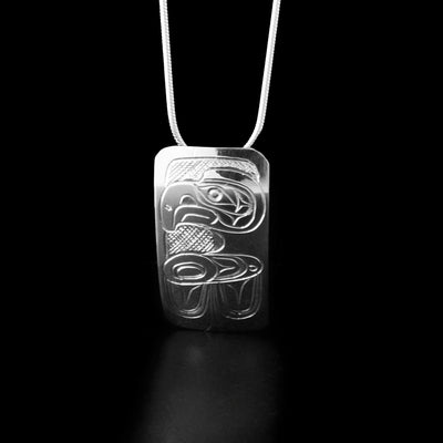 Sterling Silver Long Rectangular Eagle Pendant by Don Lancaster. The design on the pendant depicts the profile of an eagle with its head, neck, and wing facing towards the left. The eagle has a short, pointy nose and intricate designs on its head and wing to represent its feathers. The "background" has been carved into a crisscross pattern to allow for the legend to stand out.