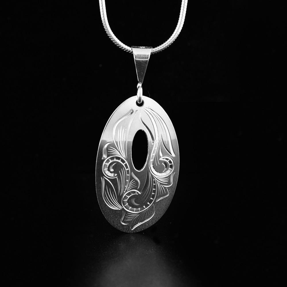 This sterling silver flower pendant is oval shaped and has a small cutout in the center of it. There are floral designs that have been carved onto the surface of the piece.