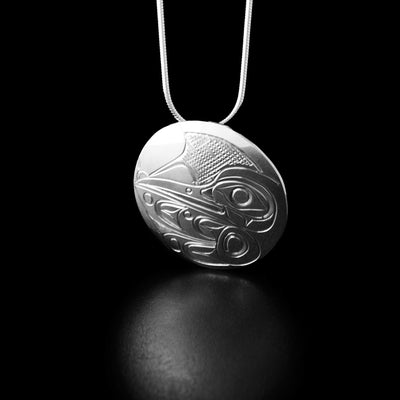 Sterling Silver Round Hummingbird Pendant by Don Lancaster. The design of the pendant depicts the profile of a hummingbird's head facing towards the left and drinking from a flower. The artist has also hand-carved a wing underneath the head of the hummingbird with intricate designs representing the feathers. The "background" of the pendant has been neatly hand-carved into a crisscross pattern to allow for the legend to stand out.
