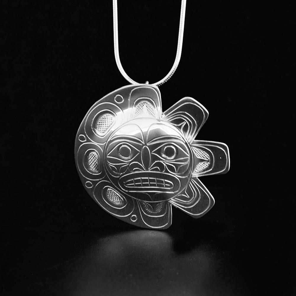 This Eclipse Sun and Moon pendant is made form sterling silver and has a large, circle shape. The pendant is shaped like and has carvings on the surafce of it depicting the Sun on one half and the Moon on the other.