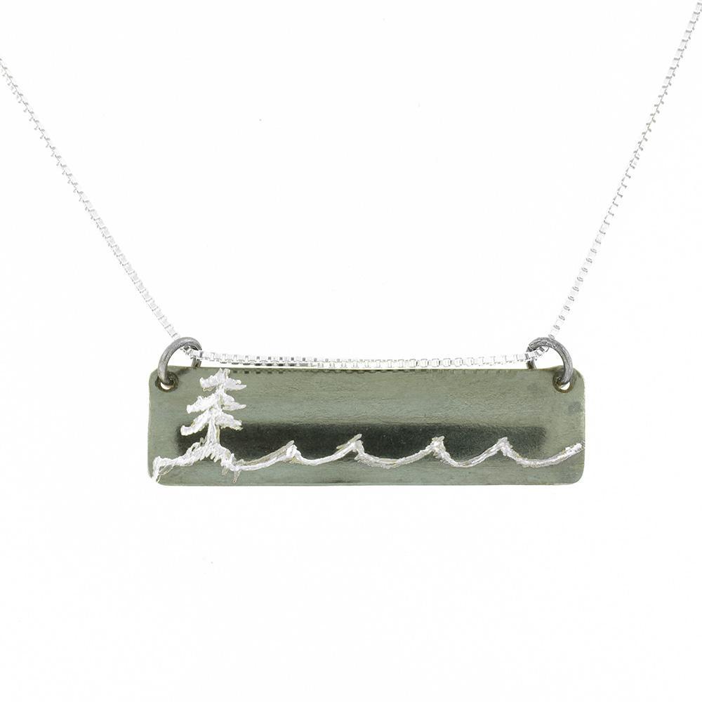 This rectangle pendant necklace is made from sterling silver and has a horizontal, thin pendant. There are carvings on the surface of the pendant that depict a tree on a coast line.