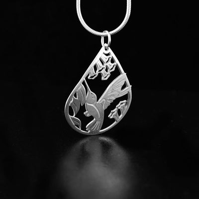 Hummingbird pendant in a teardrop shape. The design depicts a hummingbird mid-flight with flowers surrounding it and the background cut out.