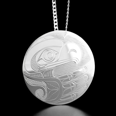 Sterling Silver Large Round Eagle Pendant by Victoria Harper. The design on the pendant depicts the profile of an eagle's head facing towards the right at the top of the pendant. The eagle has a pointy, short beak and a feather on top of its head. The artist has hand-carved a large, spread out wing with feathers underneath the head as well as a neck. The background has been neatly hand-carved into a crisscross pattern to allow for the legend to stand out.