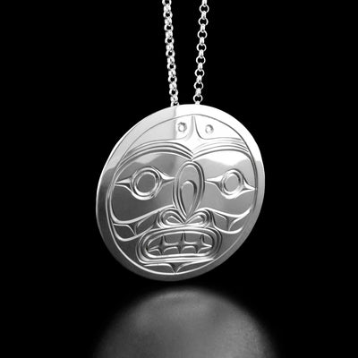 This silver moon pendant has the face of the moon in the center looking forward. The moon has a large nose and an open mouth with teeth.