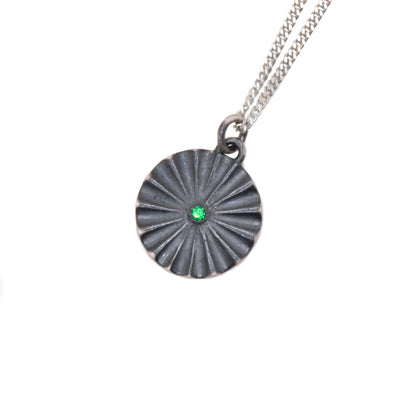 This oxidized necklace is a circular shape and is designed like a flower with petals. There is a green emerald in the center.