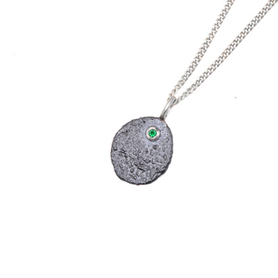 This oxidized necklace is oval in shape and is dark grey in colour with a coarse texture. There is a genuine, green emerald at the top.