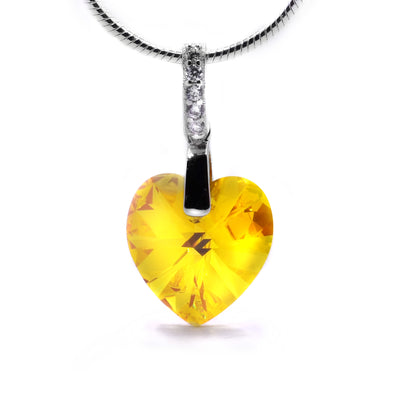 Light Topaz Swarovski Crystal Heart Pendant by Debra Nelson. The Swarovski crystal has been cut into a heart shape. The artist has handcrafted the bail and has put cubic zirconia on the bail to give it extra sine. The crystal is a "Light Topaz Swarovski Crystal", making it yellow.