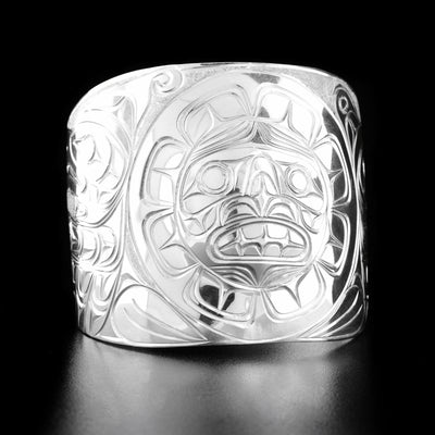 Sterling Silver 2" Eagle, Sun, and Raven Bracelet by Paddy Seaweed. The design depicts the sun looking straight in the center of the bracelet. On the left side of the bracelet is the profile of an eagle's head looking to the left with its wing spread out underneath. On the right side of the bracelet is the profile of a raven's head looking to the right with its wing spread out. The background has been delicately hand carved to allow for the legends to stand out.