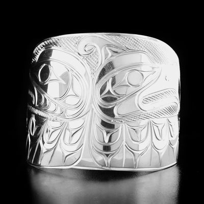 Sterling Silver 2" Thunderbird and Raven Bracelet by Paddy Seaweed. The design on one side depicts the profile of a raven's head facing the left with a wing underneath. On the other side is the profile of a thunderbird's head facing the right with a wing underneath. The background has been neatly carved to create a stark contrast with the legends.