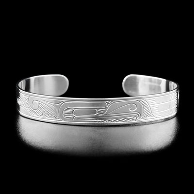 Sterling Silver 3/8" Thunderbird Bracelet by Victoria Harper. The design depicts the profile of a thunderbird's head facing towards the right in the center of the bracelet. To the right of the head the artist has hand-carved feather-like designs. To the left of the thunderbird's head the artist has hand-carved more intricate designs. In the "background" of the bracelet the artist has hand-carved a crisscross pattern to allow for the legend to stand out.