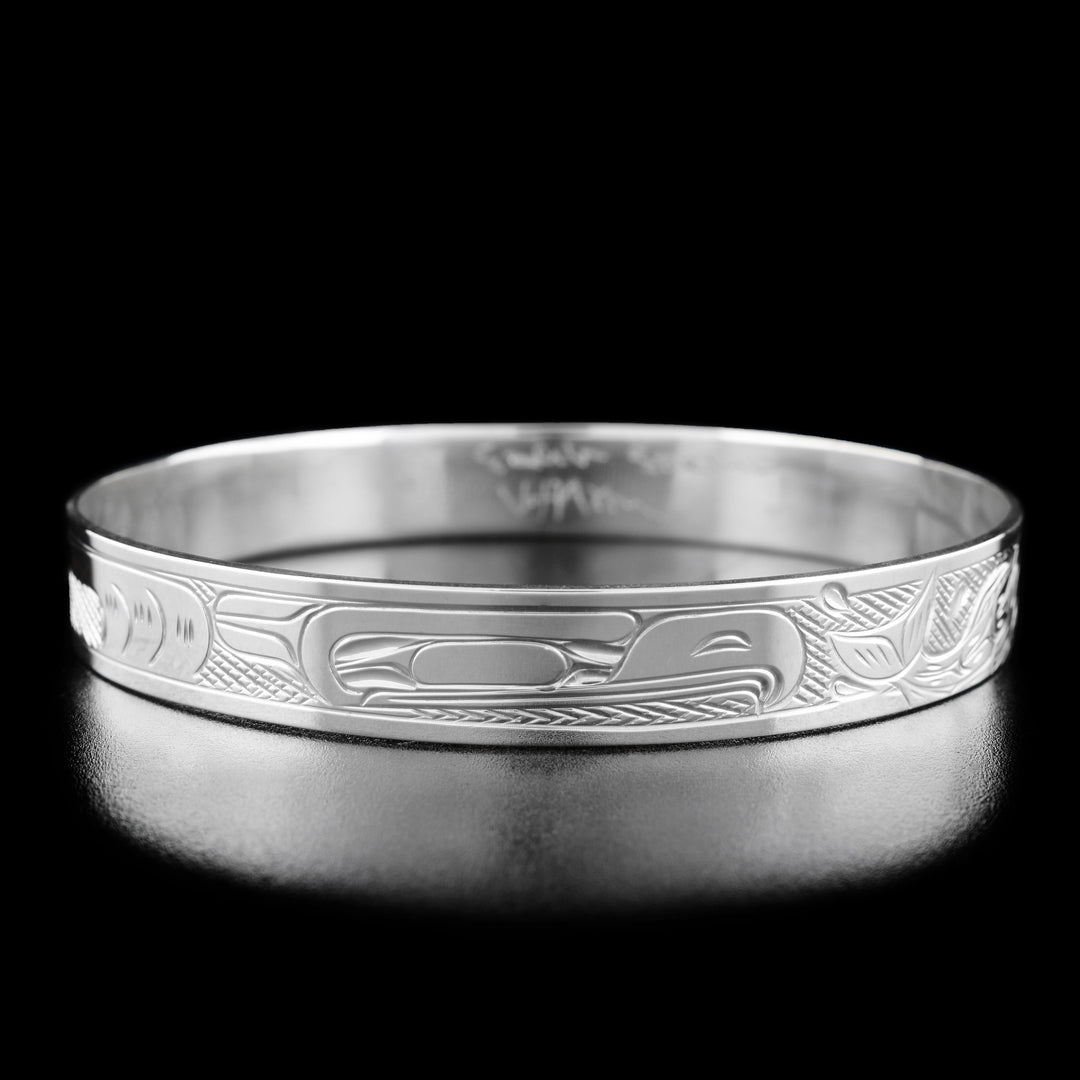 Sterling Silver 3/8" Eagle Chasing Salmon Bangle by Victoria Harper. In the center of the bracelet there is the profile of an eagle's head facing towards the right. To the right of the eagle's head there are two salmon swimming away with waves underneath them. To the left of the eagle the artist has hand-carved intricate designs to represent the eagle's feathers and body. The "background" of the bracelet has been hand-carved into a crisscross pattern to allow for the legends to stand out.