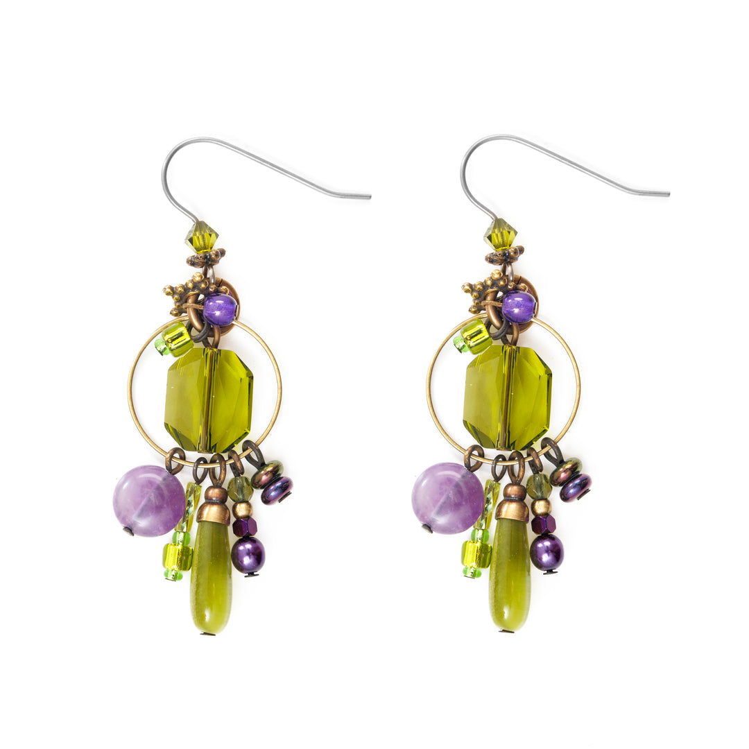 These crystal cluster earrings are made using hand worked brass, Austrian crystal, genuine amethyst, and glass beads. There are green crystal and amethyst beads run through brass wires and are dangling from the hooks and a lage brass hoop in the middle.