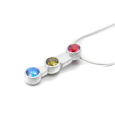 Triple Gemstone Necklace handmade by Janet Stein. The necklace is made using sterling silver along with a garnet at the top of the pendant, a garnet in the middle, and a blue topaz at the bottom. The necklace is 18" long.