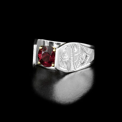 Solitaire Hummingbird Ring with Rhodolite Garnet by Fred Myra. The artist has hand-carved the profile of two hummingbird bodies on either side of the rhodolite garnet he has set in the center of the ring. The background of the ring has been hand-carved into a neat crisscross pattern to allow for the hummingbirds to stand out. The garnet has been set using a 14k gold claw setting. The ring tapers down at the back.