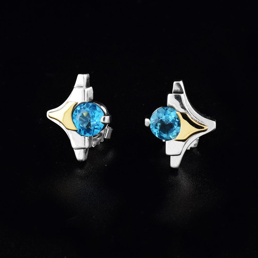These topaz stud earrings are made from sterling silver, 14K gold and blue topaz gemstones. The studs are shaped like diamonds and have gold and silver layered designs with topaz gemstones held in the center of them.