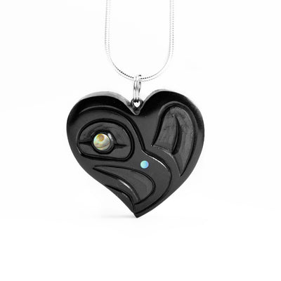 Argillite Eagle Heart Pendant by Amy Edgars. The pendant is in the shape of a lopsided heart. In the center the artist has hand-carved the profile of an eagle's head facing towards the right on the left side of the heart. She has but abalone in the eagle's eye and beak. On the right side of the pendant the artist has hand-carved an intricate design representing the feather of the eagle.