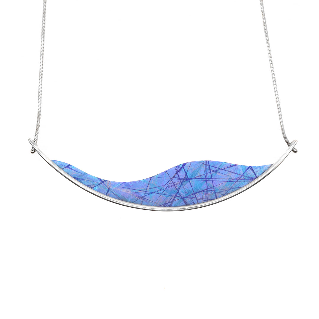 This titanium necklace with pendant has been made using sterling silver and anodized titanium. There is a long and wavy titanium piece that has a light blue color and dark blue/purple designs on the surface of it achieved by anodizing the metal. The titanium piece is held with a silver wire that extends past the piece.