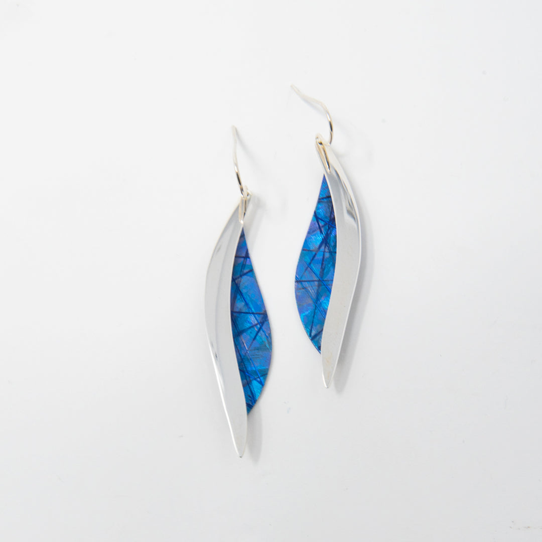 These titanium earrings are made from sterling silver and anodized titanium. There are curved, sterling silver wires dropping down with teardrop shaped titanium hangs at the bottom. The titanium is blue and has colorful designs achieved by anodizing the metal.
