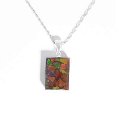 Pendant by Aryn Bowers. He has encased flakes of ammolite in resin to create it. Double-sided, each side has a unique display of ammolite. Sterling silver bail. Pendant measures 1" x 0.5" including bail.