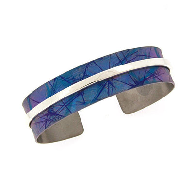 Medium Blue Titanium Bracelet by artist Jean-Yves Nantel. Simple, yet elegant, this blue cuff bracelet is enhanced with a narrow strip of sterling silver. Bracelet shown is a medium. It is 6.19" long with a 0.94" gap and has a width of 0.56". Please inquire with us about other available sizes.