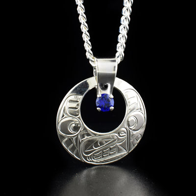 Round Bear Cut Out Pendant with Blue Stone hand-carved by Coast Salish and Cree artist Richard Lang. Made of sterling silver and a lab-created blue stone. Pendant measures 1.44" x 1.19" including bail. Chain not included.