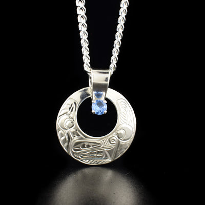 Round Wolf Cut Out Pendant with Aquamarine Stone hand-carved by Coast Salish and Cree artist Richard Lang. Made of sterling silver and a lab-created aquamarine-coloured stone. Pendant measures 1.44" x 1.19" including bail. Chain not included.
