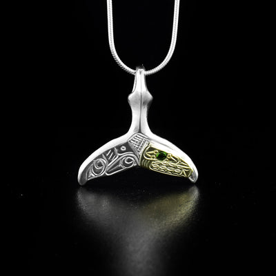 Stunning whale tail pendant hand-carved by Coast Salish and Cree artist Richard Lang. The orca's face is done in 14K gold and the rest of the piece is made of sterling silver. Richard has set a dark green lab-created stone in the eye of the orca. Pendant measures 1.5" x 1". Chain not included.