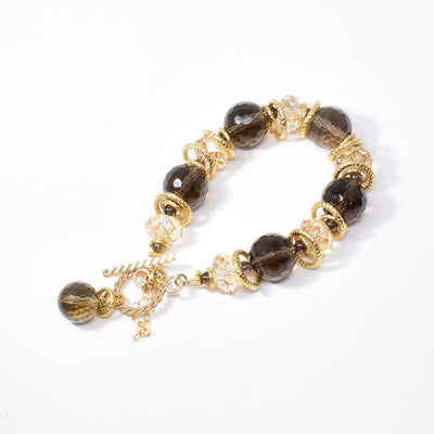Smoky Quartz and Swarovski Crystal Bracelet handcrafted by artist Karley Smith. She used gold-plated rings, smoky quartz, Swarovski Crystal in Golden Shadow and gold-filled finishing to create this dazzling piece. Bracelet closes with a toggle clasp and a safety chain adds an extra element of security. Bracelet is 7.25" long.