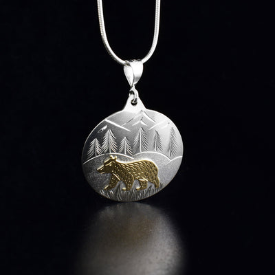Sterling silver and 10K gold bear in the woods pendant hand-carved by artist Brett Borrie. Pendant measures 1.75" x 1". Chain not included.