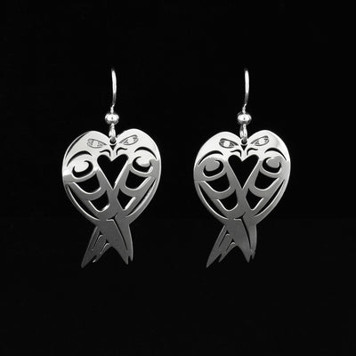 Sterling Silver Lovebird Earrings by Grant Pauls. Each earring has a shape similar to that of a heart. Each earring is made up of two lovebirds facing towards each other. The artist has cut out parts of the lovebirds body and wings to represent the feathers. 