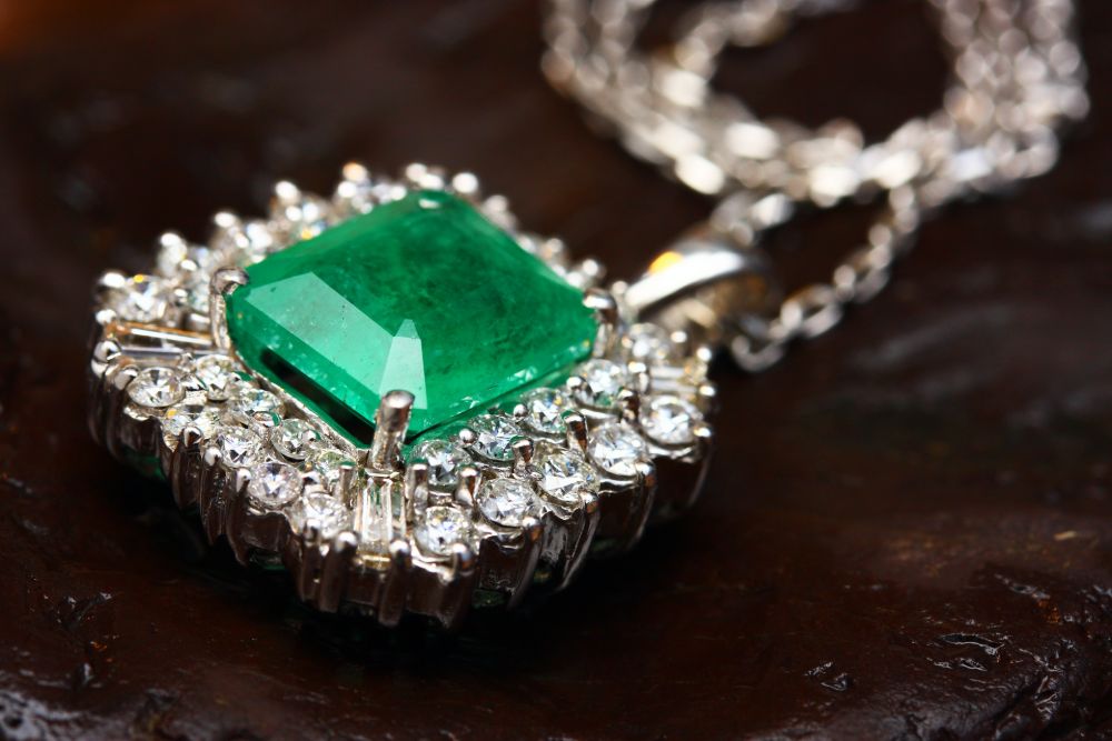 Emerald pendant necklace with diamonds surrounding square stone.