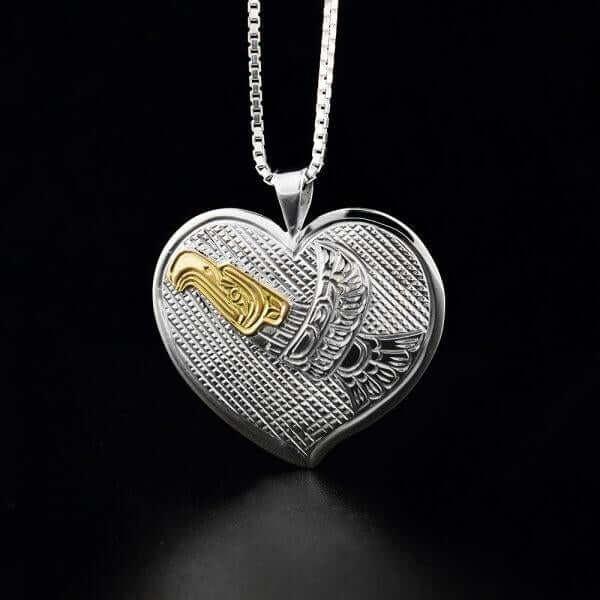 The image shows a gold & silver eagle carved on a silver heart shape pendant. It is a beautiful indigenous jewelry art, symbolizing eagle legend. 
