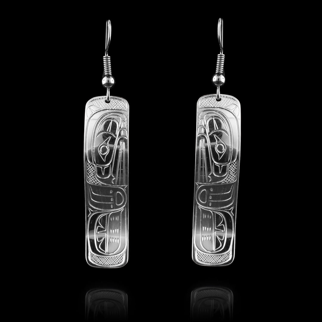 These rectangle dangle earrings have long, rectangle hangs with rounded edges that are made from sterling silver. a depiction of the Bear legend is carved into the hangs. The head of the Bear is at a side profile and looking downward with its paw at the bottom of the piece. The hangs have been bent to have a wavy shape.
