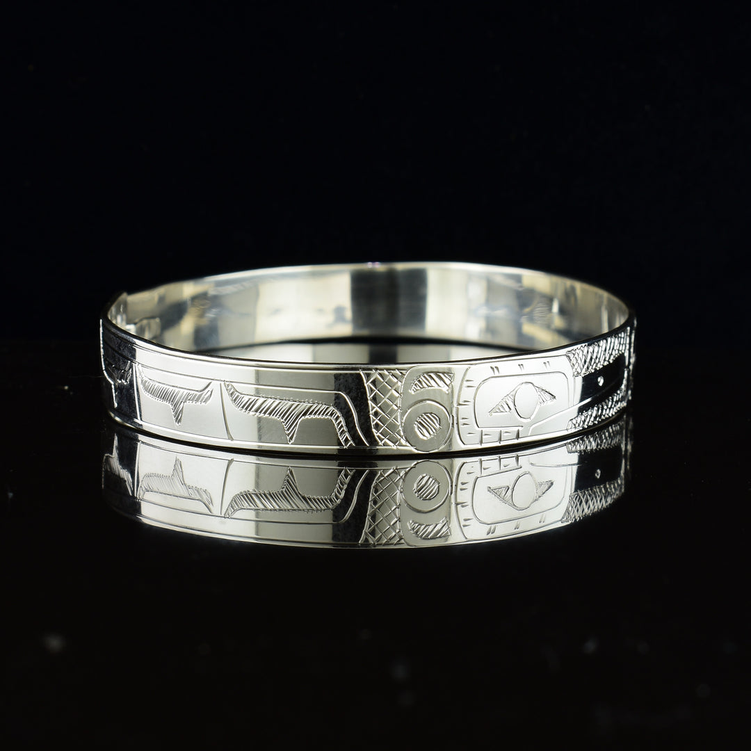 These sterling silver bangle bracelets have a single, thin band with a hook clasp in the back. There are depictions of the Eagle and the Hummingbird legends carved into either side of the band. The legends are depicted facing each other and where their heads meet, in the center, the Moon legend is depicted between them.