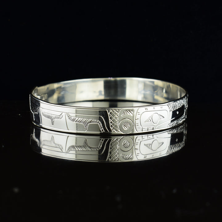 These sterling silver bangle bracelets have a single, thin band with a hook clasp in the back. There are depictions of the Eagle and the Hummingbird legends carved into either side of the band. The legends are depicted facing each other and where their heads meet, in the center, the Moon legend is depicted between them.