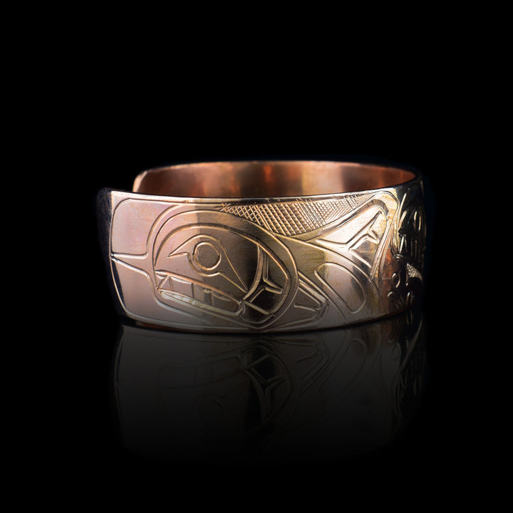 This copper cuff bracelet has a wide band with a depiction of three, Orca whales carved into the surface of it. The whales are done at a side view and are breaching with their heads and Doral fins shown. There are splashing designs of the ocean made around the Orca pod.