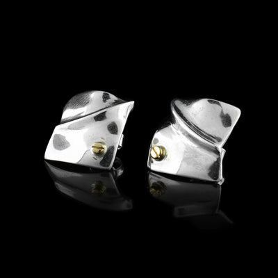 These abstract stud earrings have square shaped studs mad from sterling silver. The studs are convex and there is a ridge going across them. There is a 14K gold stud in the top of the corner.