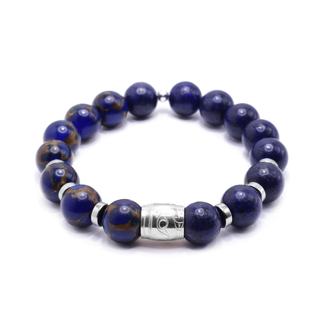 This gemstone charm bracelet has small, sphere shaped beads made from jasper and reconstructed lapis. The jasper beads have a blue color with brown highlights. There is a sterling silver spirit bead in the center of the piece with a depiction of the head of the Raven carved into it. There are round, flat silver spacers (three on either side of the spirit bead).