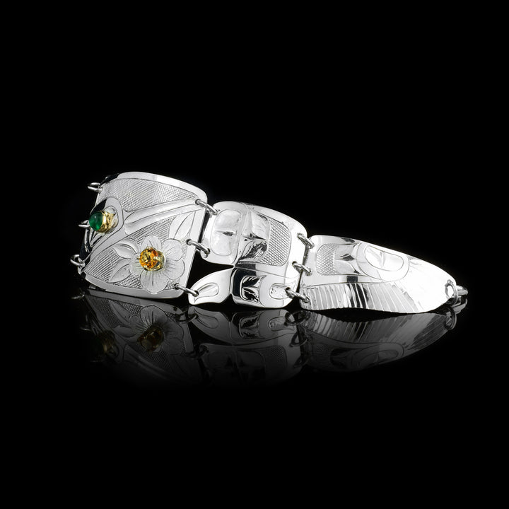This panel bracelet is made from sterling silver and has a wide, center panel with two, tapered pieces on each side of it. There is a depiction of the Hummingbird with a flower in the center, designs on the second one, and the end pieces depict the wings of the legend. There is a green onyx gem in the eye of the legend and a citrine gem in the flower.