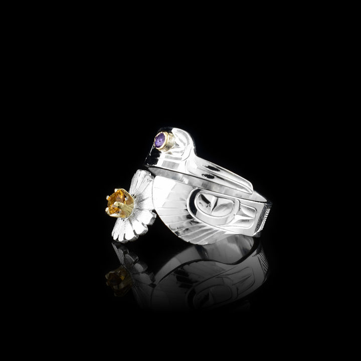 This Hummingbird ring is made from sterling silver and has a single band that wraps around the finger twice. There are carvings on the sirafec of the piece depicting the Hummingbird. The head is on the top and the wing with a daisy is at the bottom. There is an amethyst gem in the eye and a citrine gem in the center of the flower.